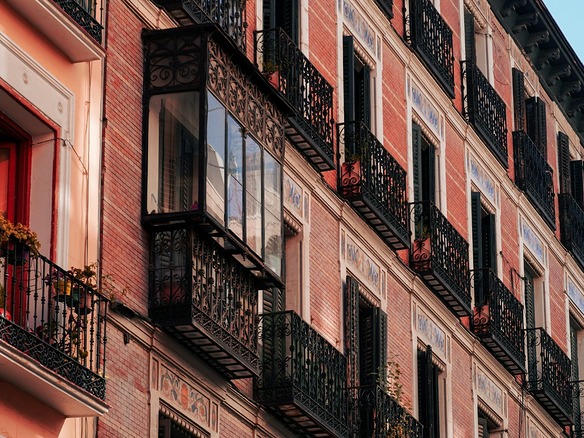 Fachada de ladrillo con balcones de hierro forjado, miradores acristalados y azulejos decorativos, iluminada por la luz dorada del atardecer.