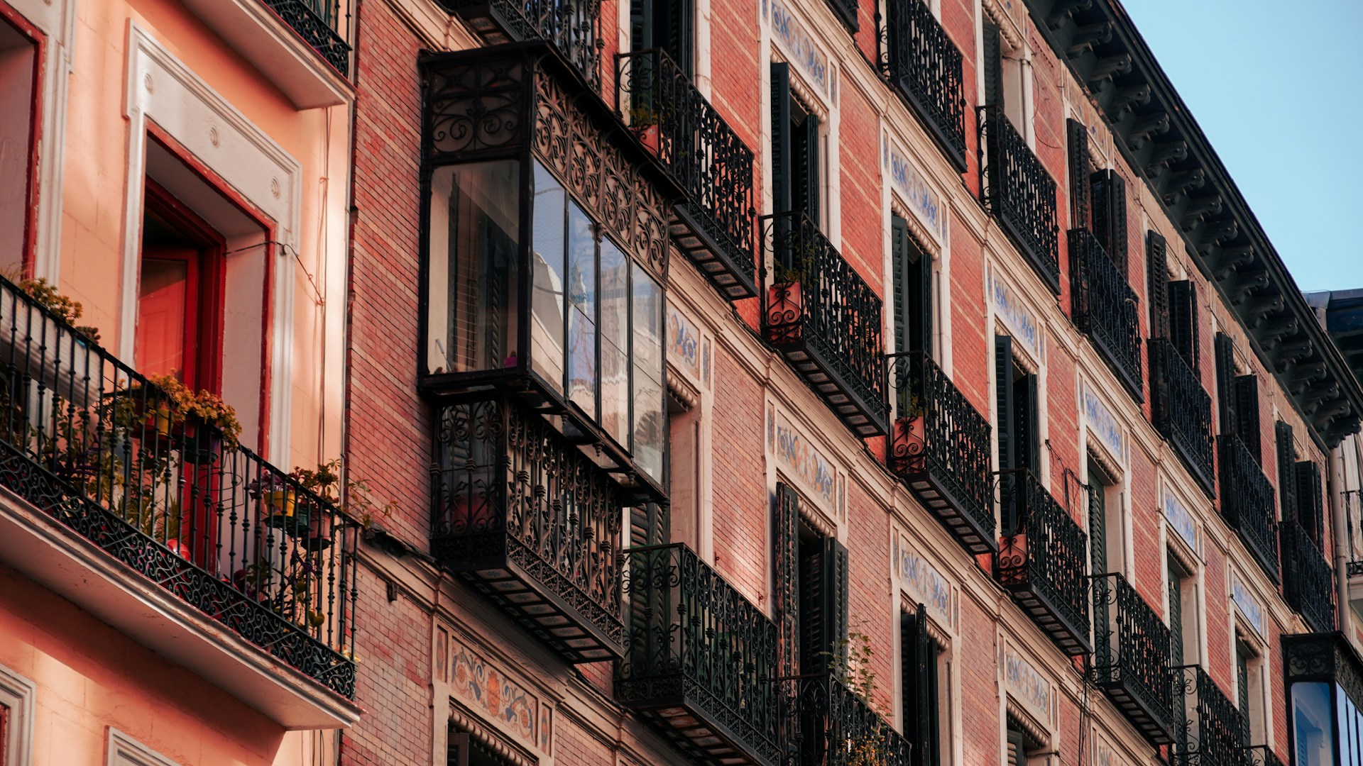 Fachada de ladrillo con balcones de hierro forjado, miradores acristalados y azulejos decorativos, iluminada por la luz dorada del atardecer.