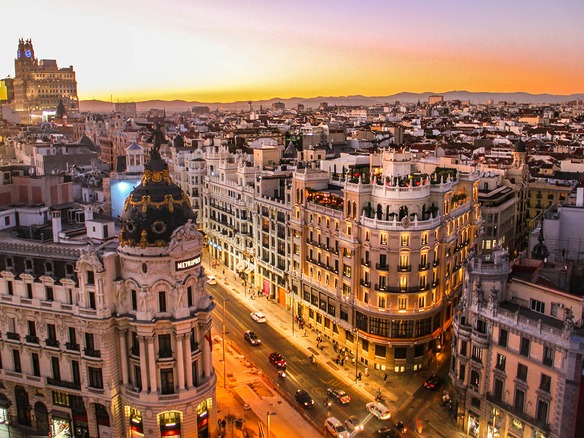 Vista elevada de la Gran Vía de Madrid al atardecer, con el edificio Metrópolis, terrazas en las azoteas y fachadas iluminadas