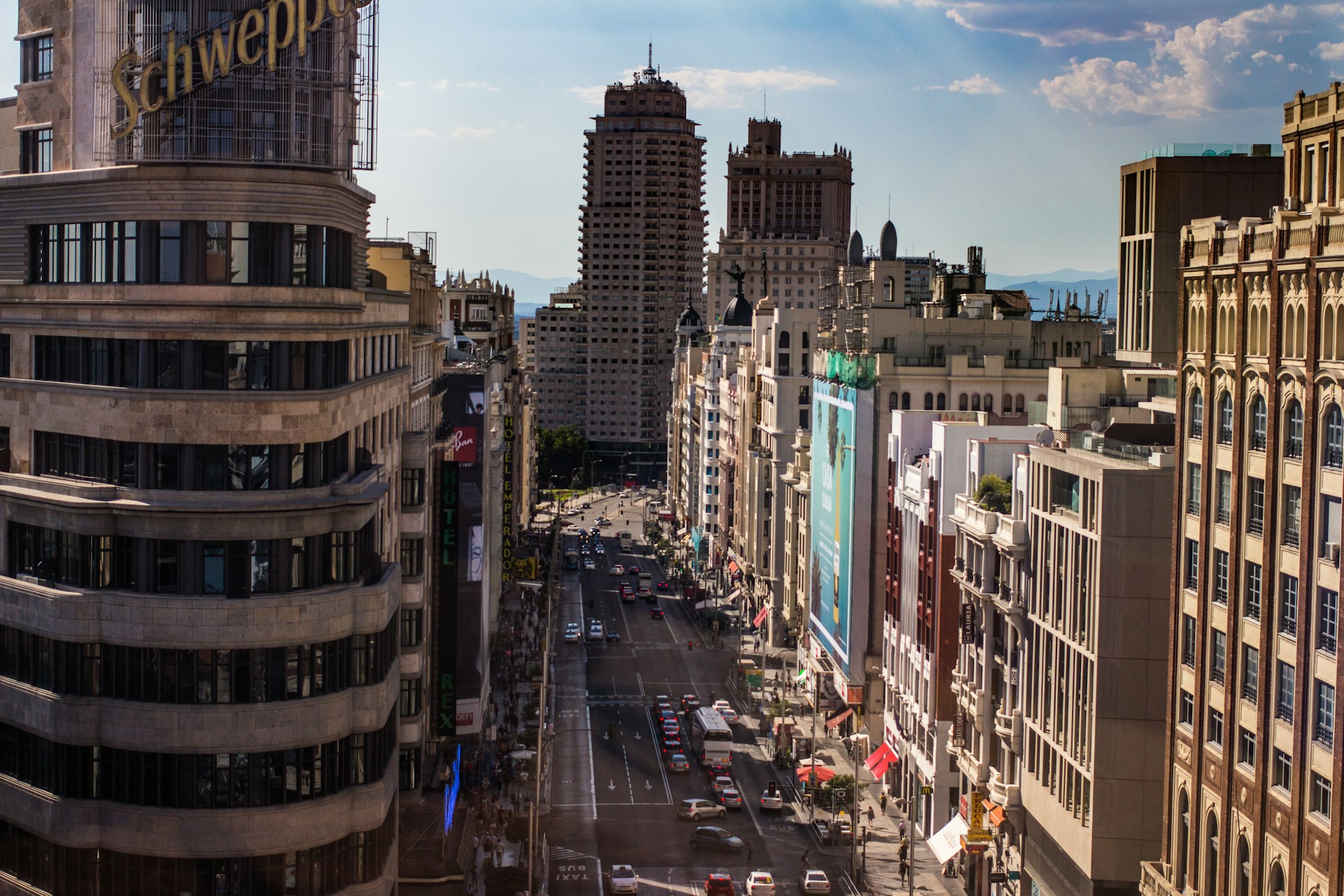 Vista elevada de la Gran Vía de Madrid a media tarde, con tráfico, aceras concurridas y fachadas históricas bajo el sol