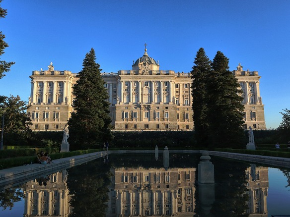 Luz cálida de tarde en los Jardines de Sabatini de Madrid: el Palacio Real, el estanque en calma y dos personas sentadas al borde.