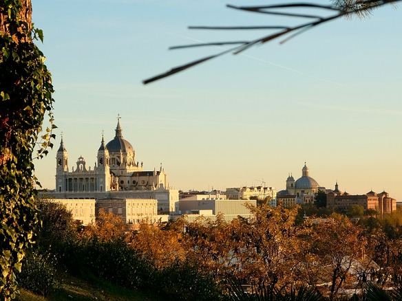 Cúpulas y campanarios del centro de Madrid al atardecer, vistos por encima de una ladera de árboles con hojas doradas y cobrizas.