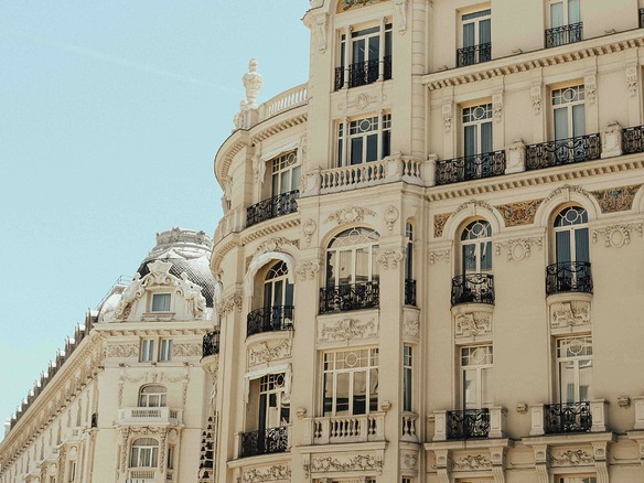 Fachada señorial madrileña con balcones de hierro forjado, molduras ornamentadas y una cúpula de pizarra, bajo el sol