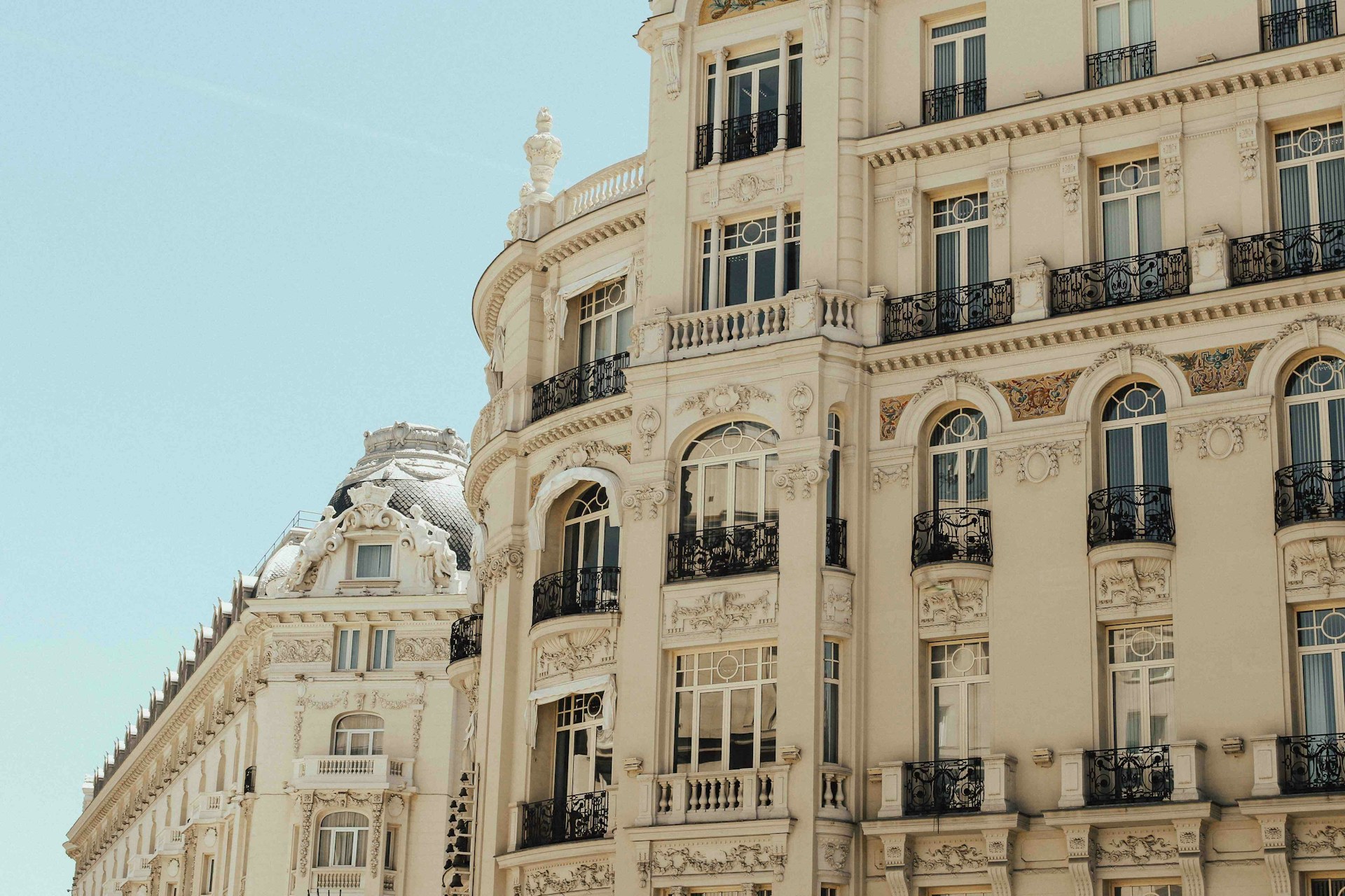 Fachada señorial madrileña con balcones de hierro forjado, molduras ornamentadas y una cúpula de pizarra, bajo el sol