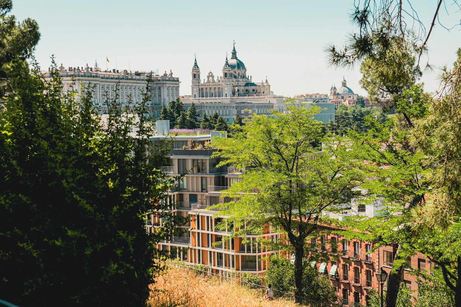 Vista de Madrid con el Palacio Real y la catedral de la Almudena al fondo, arboledas verdes y bloques de viviendas con terrazas