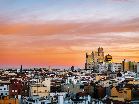 Panorámica de los tejados de los barrios residenciales de Madrid al anochecer con cielo anaranjado y la torre de Telefónica al fondo