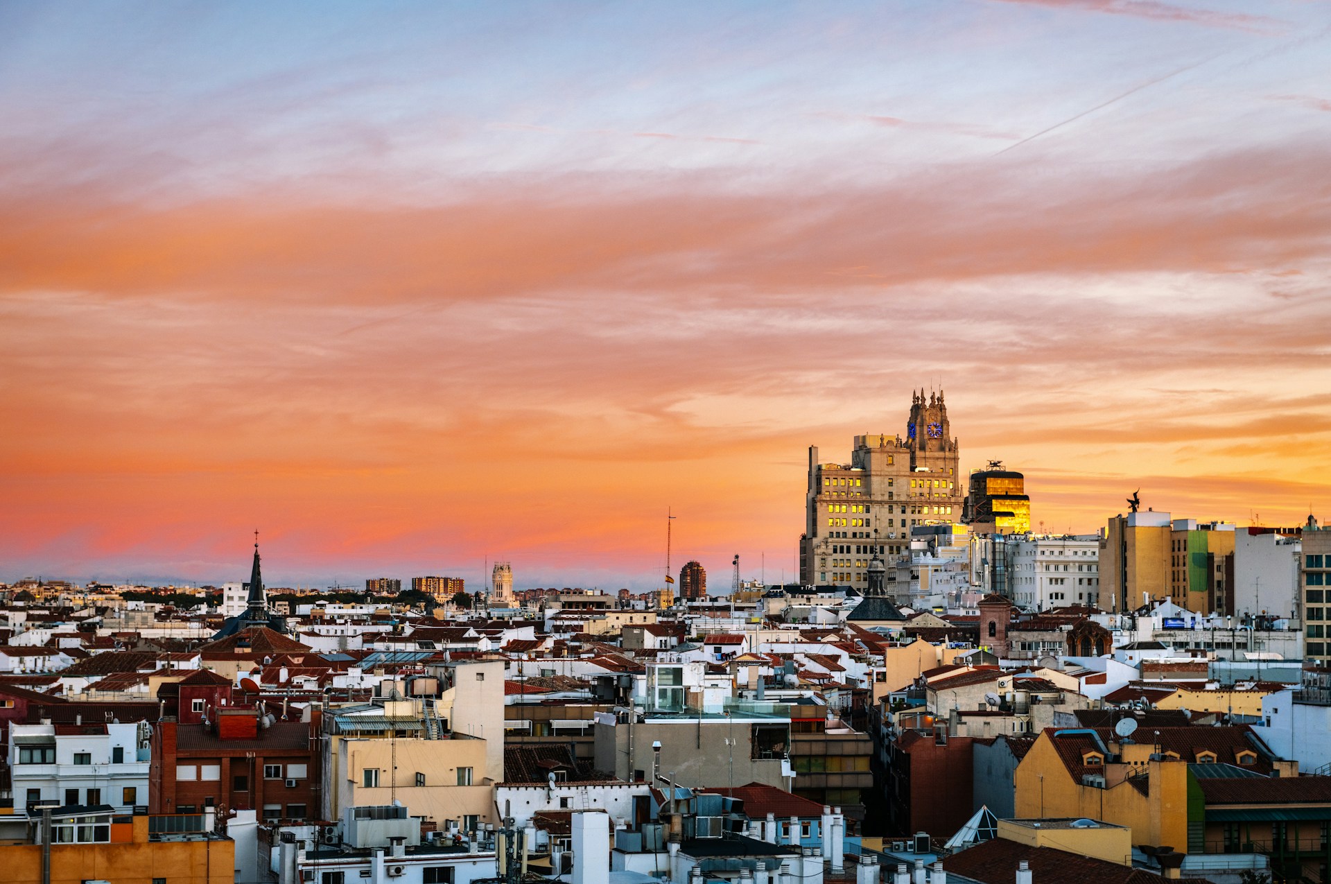 Panorámica de los tejados de los barrios residenciales de Madrid al anochecer con cielo anaranjado y la torre de Telefónica al fondo